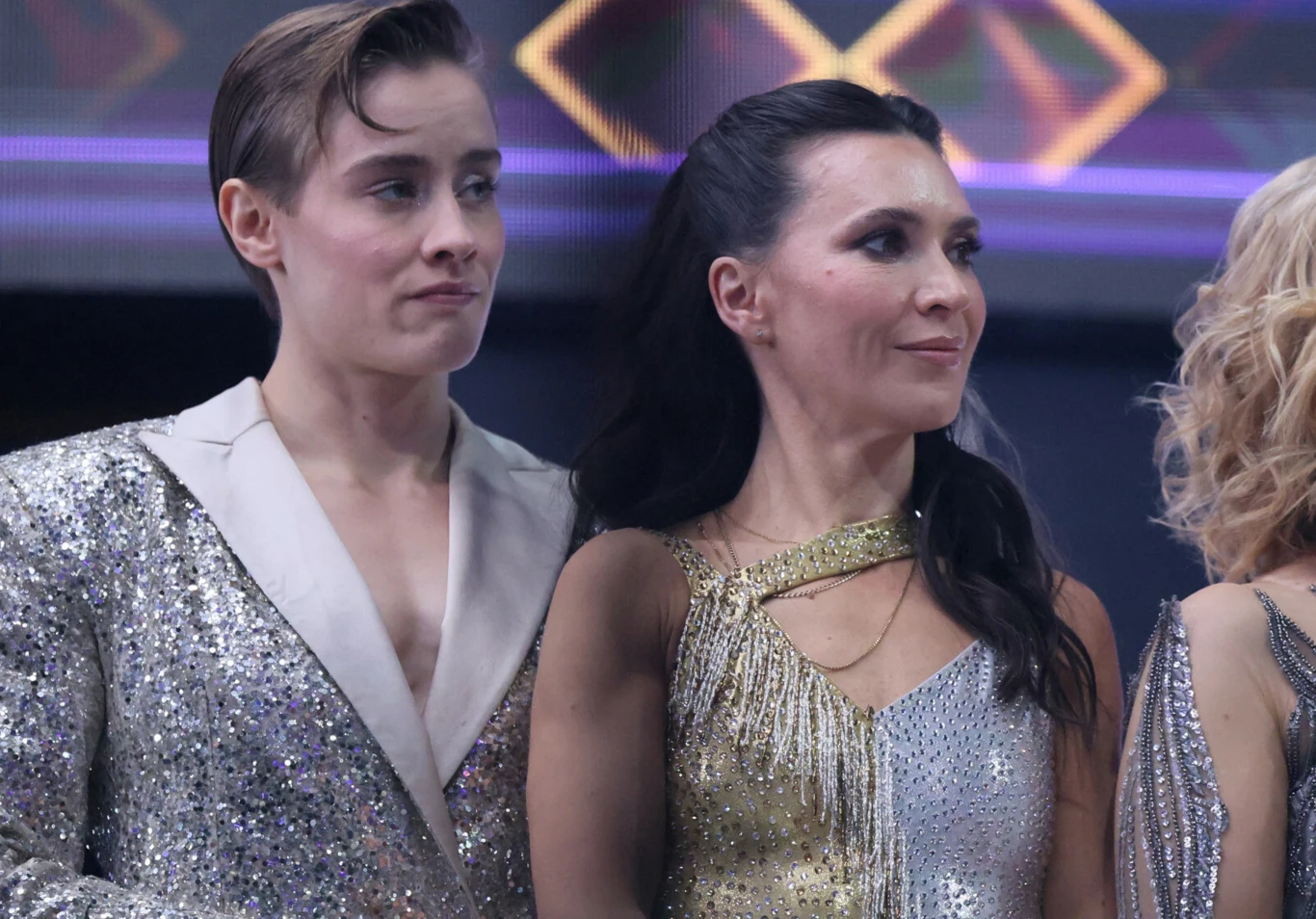 Katarzyna Zillmann, Janja Lesar Dwie osoby stojące obok siebie w błyszczących, srebrnych i złotych strojach scenicznych z eleganckimi fryzurami, w tle geometryczne wzory w jasnych kolorach.