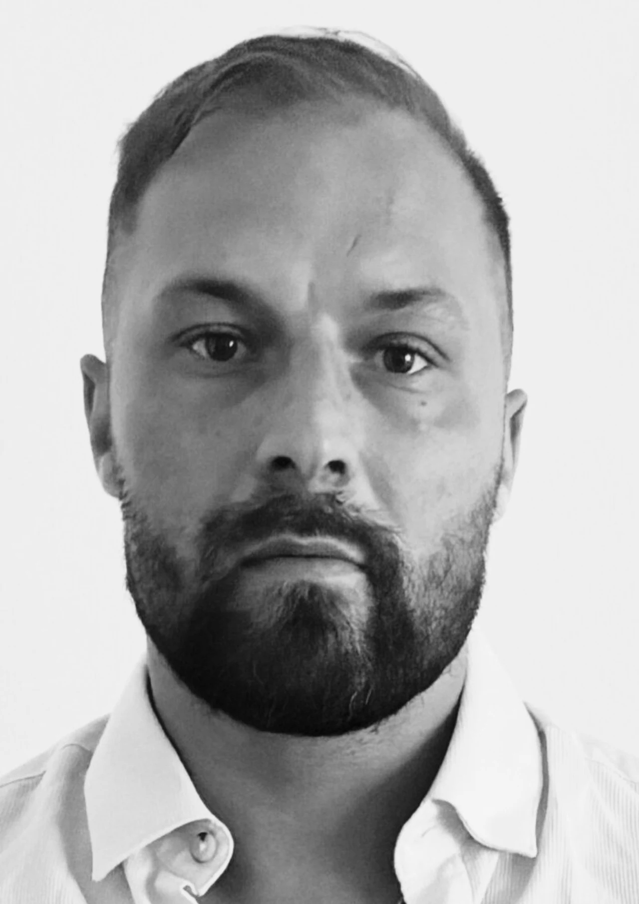 Znaleziono ciało 34-letniego Marka Kubaczki. Policja bada przyczyny śmierci mężczyzny Mężczyzna o krótkich włosach i brodzie, w białej koszuli, patrzy prosto w obiektyw na jasnym tle.