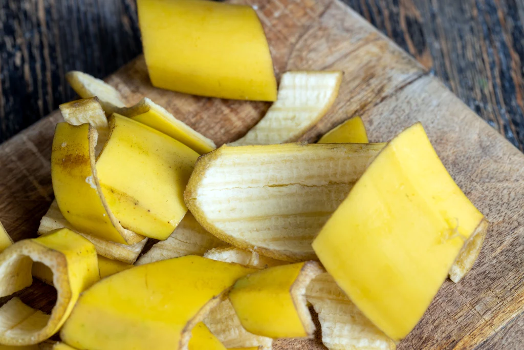 Pokrojone na kawałki żółte skórki od banana leżą na drewnianej desce, tło stanowi drewniana powierzchnia.