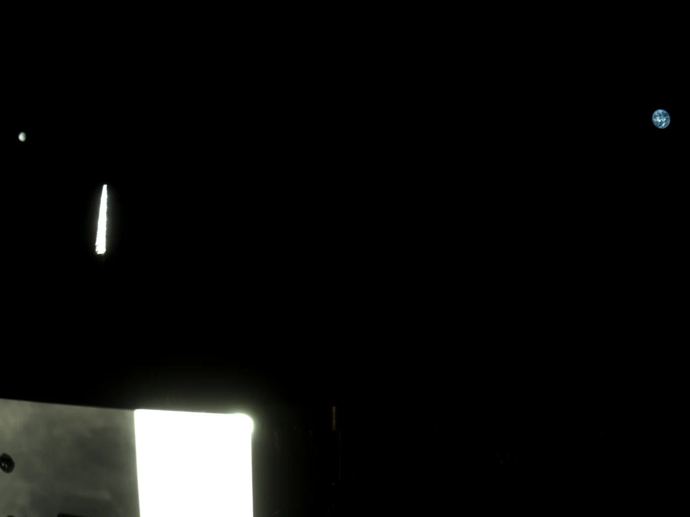 Czarna przestrzeń kosmiczna, na pierwszym planie fragment oświetlonego urządzenia lub sondy kosmicznej, w górnym rogu widoczna planeta Ziemia na tle ciemnego nieba.