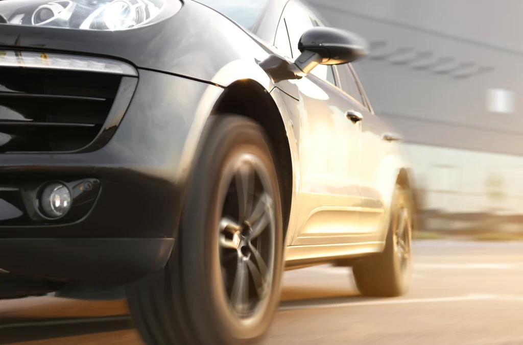 Luksusowy czarny samochód osobowy w ruchu, ujęcie z niskiej perspektywy skupiające się na przednim kole i zderzaku, z rozmazanym tłem sugerującym prędkość.