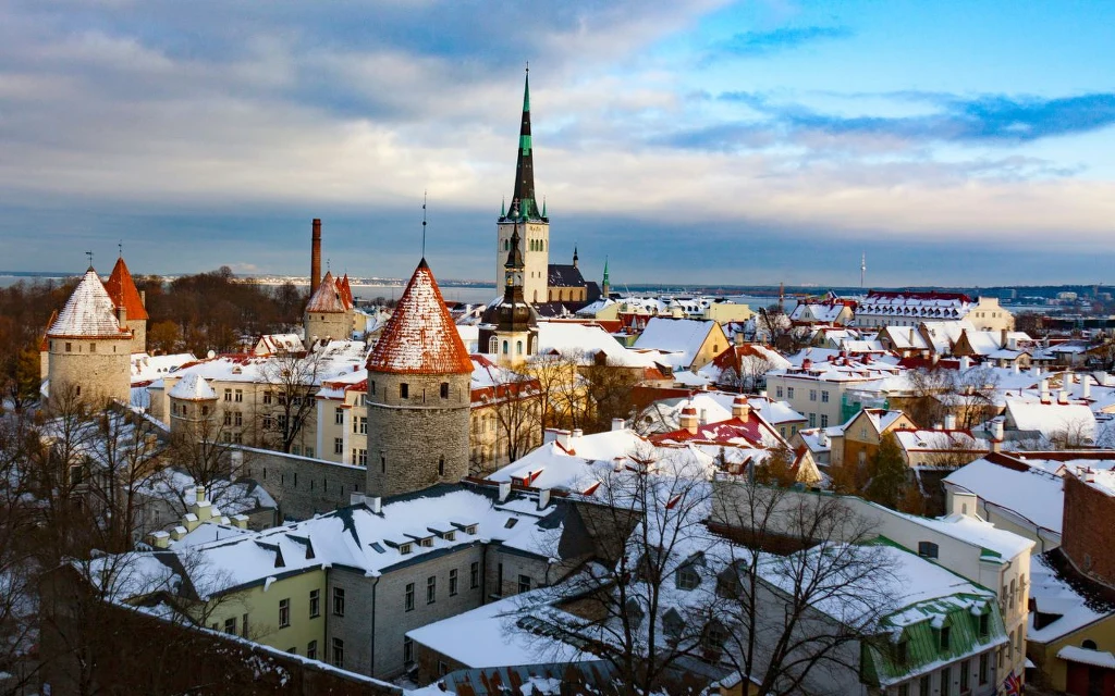 Stare miasto z widocznymi murami obronnymi, licznymi wieżami oraz wysokim kościołem na tle śnieżnych dachów i błękitnego nieba.