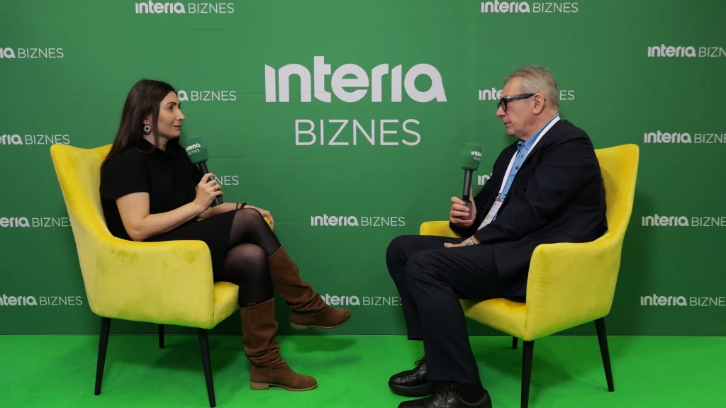 Rozmowa dwóch osób siedzących naprzeciwko siebie na żółtych fotelach, każda trzyma mikrofon. W tle zielona ścianka z napisem interia BIZNES.