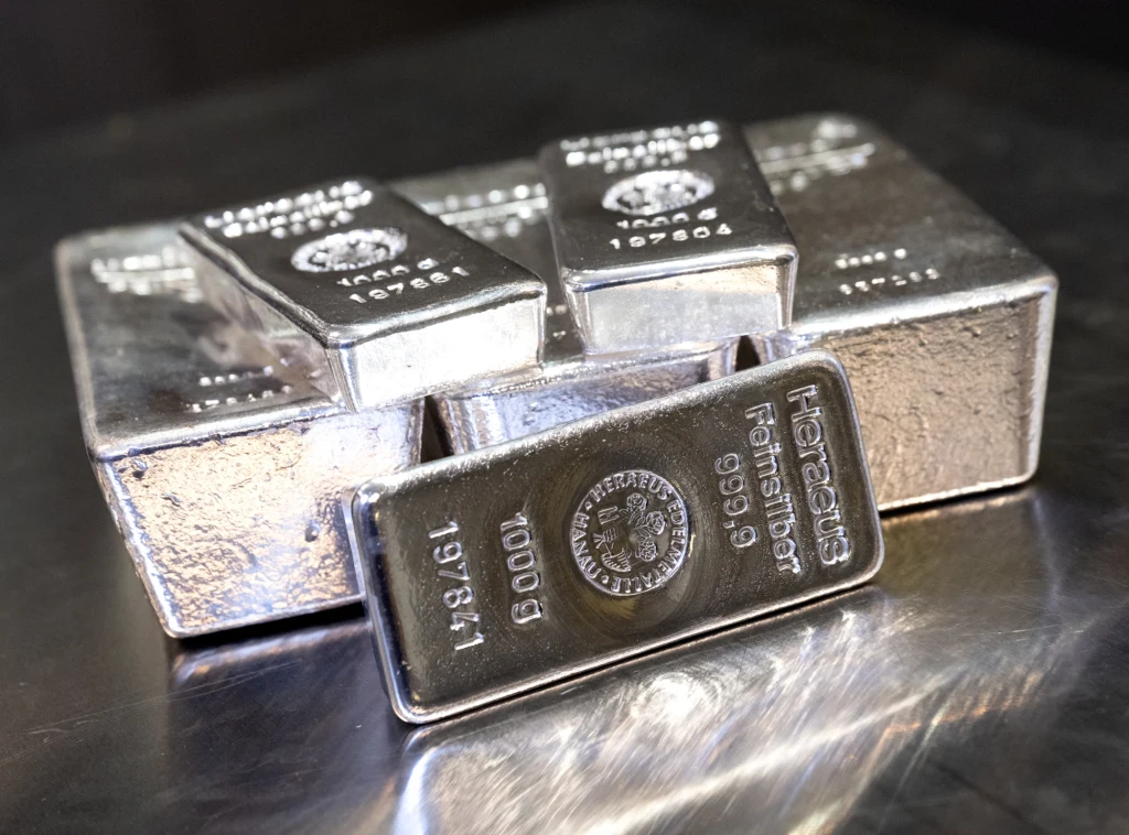 Kilka srebrnych sztabek ułożonych na metalicznej powierzchni, każda z wyraźnym oznaczeniem producenta, wagą oraz próbą srebra.