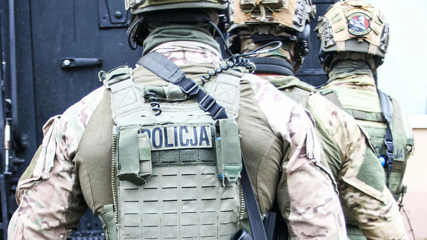 Zorganizowana grupa rozbita. Wśród oskarżonych były funkcjonariusz policji (zdj. ilustracyjne) Trzech funkcjonariuszy oddziału specjalnego policji w kamuflażowych mundurach i hełmach ochronnych stoi przed wejściem do budynku. Na plecach jednego z nich widoczny napis POLICJA.