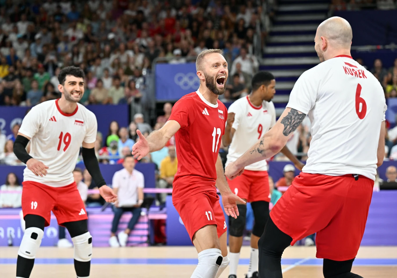 Polscy siatkarze świętują zdobycie punktu podczas meczu na hali sportowej, wokół nich kibice na trybunach, a atmosfera jest pełna radości i sportowej energii.