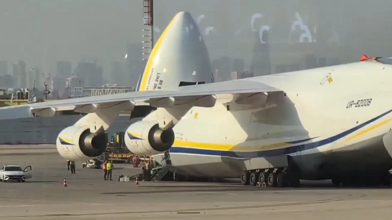 Ukraiński An-124 wylądował w Izraelu. Zabrał na pokład potężną broń Największy na świecie samolot transportowy Antonow An-225 Mrija stojący na płycie lotniska, z podniesioną częścią dziobową umożliwiającą załadunek, w otoczeniu kilku osób oraz pojazdu serwisowego, w tle majaczy panorama miasta.
