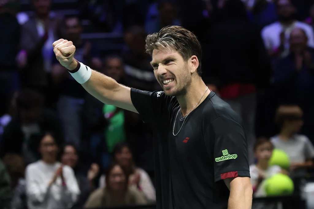 Cameron Norrie Sportowiec ubrany w czarną koszulkę z zaciśniętą pięścią wyrażającą triumf lub determinację, w tle widownia o niewyraźnych twarzach.