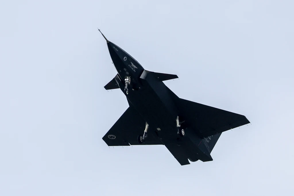 Turcja dokonała niemożliwego. Stworzyli drona, który sam może niszczyć dalekie cele Czarny myśliwiec odrzutowy lecący na tle jasnego, bezchmurnego nieba z wysuniętym podwoziem.