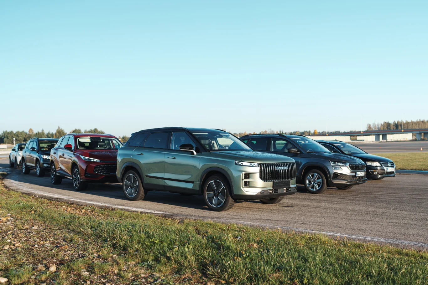 Nowy chińczyk, używany Passat, a może Skoda, Kia lub Toyota? Sprawdziliśmy drogę hamowania i sprawność systemów bezpieczeńśtwa. Wyniki dają do myślenia Sześć nowoczesnych samochodów osobowych ustawionych w rzędzie na torze testowym, w otoczeniu zieleni i asfaltowej nawierzchni, przy jasnym, słonecznym niebie.
