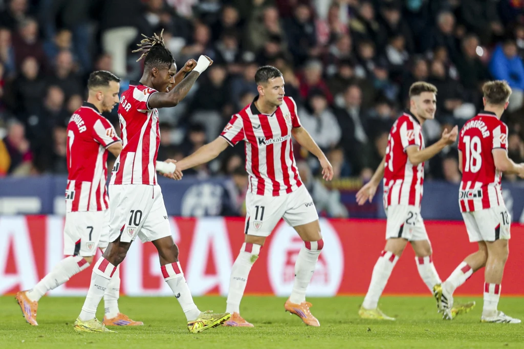 Piłkarze Athletiku Bilbao w sezonie 2025/2026 Grupa piłkarzy w czerwono-białych koszulkach świętuje zdobycie gola na murawie stadionu, otoczona przez kibiców na trybunach, pełnych emocji i energii sportowej.
