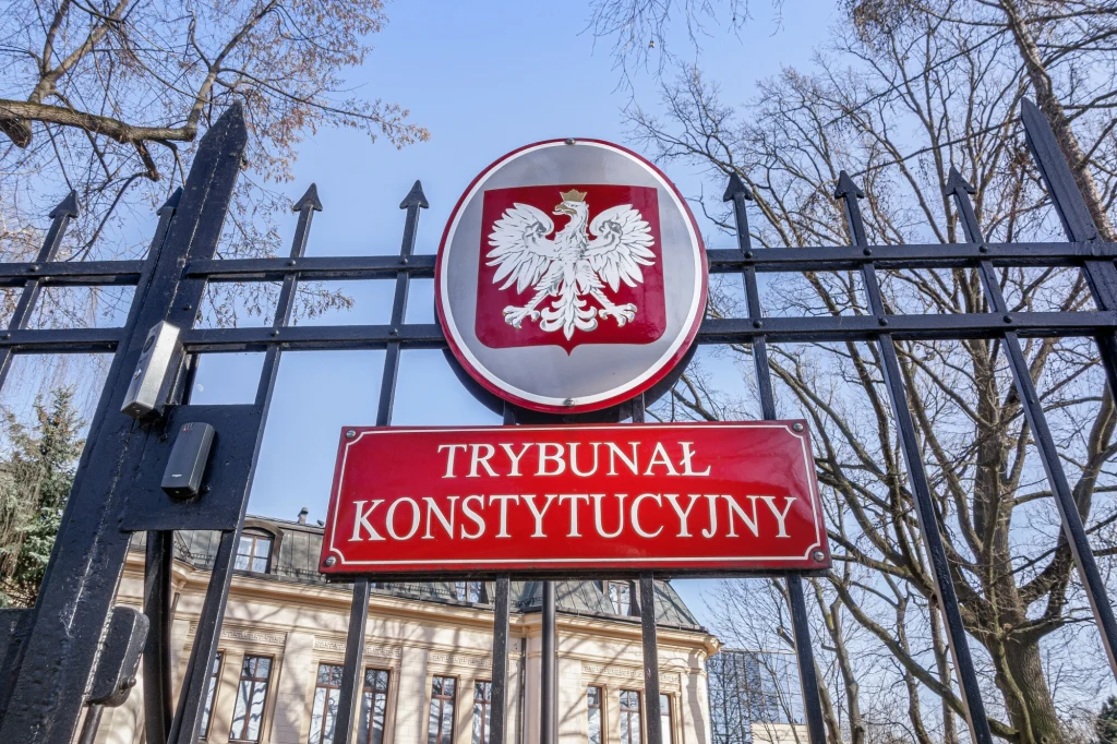 Trybunał Konstytucyjny ogłosił wyrok dotyczący braku prawa do ponownego przeliczenia emerytur mieszanych Tablica z napisem 'Trybunał Konstytucyjny' i godłem Polski umieszczona na metalowym ogrodzeniu, w tle widać fragment budynku i bezlistne drzewa.