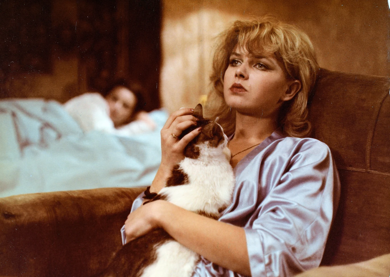 Maria Probosz marzyła o karierze na miarę Marilyn Monroe Kobieta w jedwabnym szlafroku siedzi na fotelu i przytula kota, w tle leży druga osoba przykryta kołdrą na łóżku. Atmosfera intymności i zamyślenia.