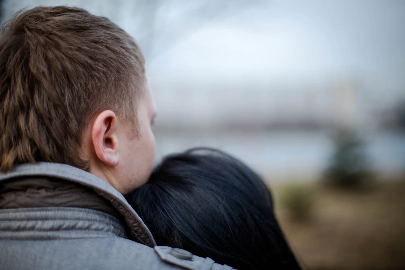 Para wtulona w siebie na świeżym powietrzu, mężczyzna obejmuje kobietę, głowa kobiety oparta na jego ramieniu, tło rozmyte i nieostre.