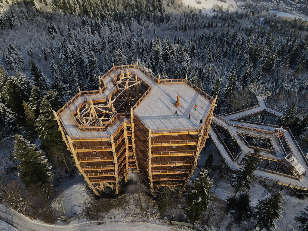 W Wiśle otwarto nową wieżę widokową. To pierwsza tego typu atrakcja w Beskidzie Śląskim. Drewniana wieża widokowa w otoczeniu ośnieżonego lasu, z drogą prowadzącą do platformy widokowej. Konstrukcja składa się z kilku poziomów i ścieżek, po których spacerują pojedyncze osoby. W tle rozciąga się panorama zimowego krajobrazu.