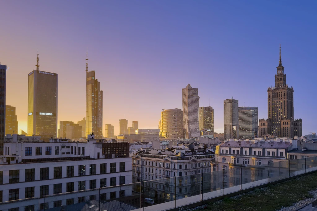 OECD prognozuje, że PKB Polski w 2026 r. wzrośnie o 3,4 proc., a w 2027 r. o 2,7 proc. Panorama centrum Warszawy o zmierzchu z wyraźnie widocznymi drapaczami chmur, w tym charakterystycznym Pałacem Kultury i Nauki, na tle nieba przechodzącego od żółtego po błękitne barwy.