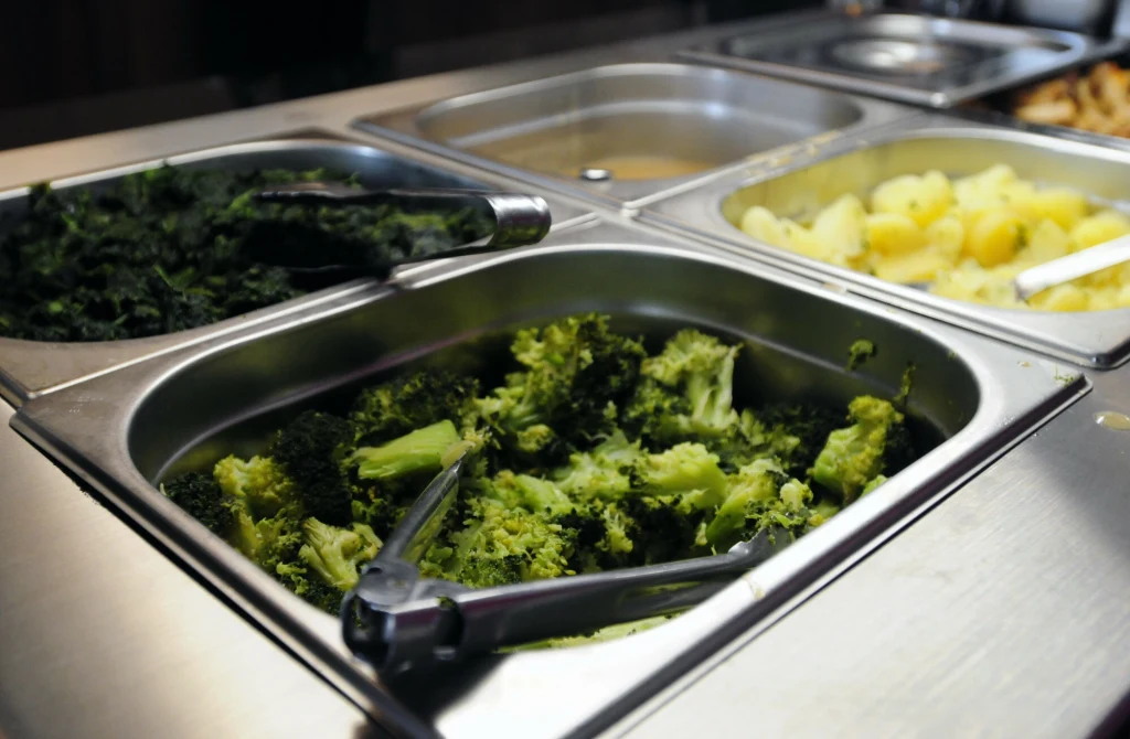 Za granicą są już szpitale, które wprowadzają menu roślinne jako opcje pierwszego wyboru Podgrzewacze z gorącymi daniami w stołówce, w których widoczne są brokuły, szpinak oraz ziemniaki. Metalowe szczypce służą do nakładania warzyw.