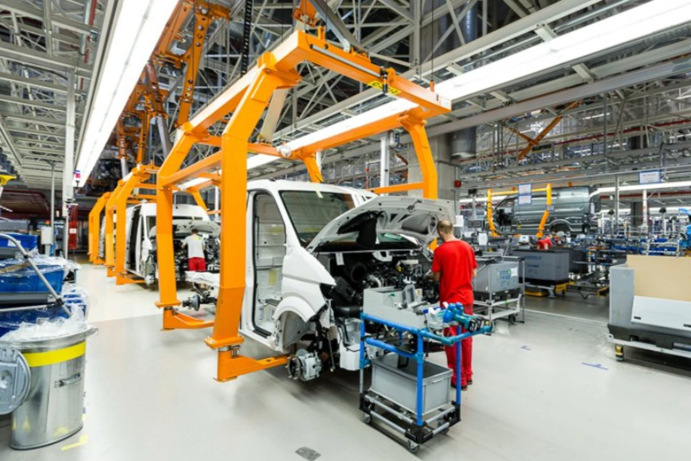 Czy modernizacja zakładu Volkswagen Poznań we Wrześni pomoże firmie toczyć walkę na dwóch frontach? Mają tam stanąć dwie zupełnie nowe hale Hala produkcyjna z nowoczesną linią montażową pojazdów dostawczych, pracownik w czerwonym stroju obsługujący pojazd w trakcie składania, otoczenie wypełnione częściami samochodowymi i elementami konstrukcyjnymi.