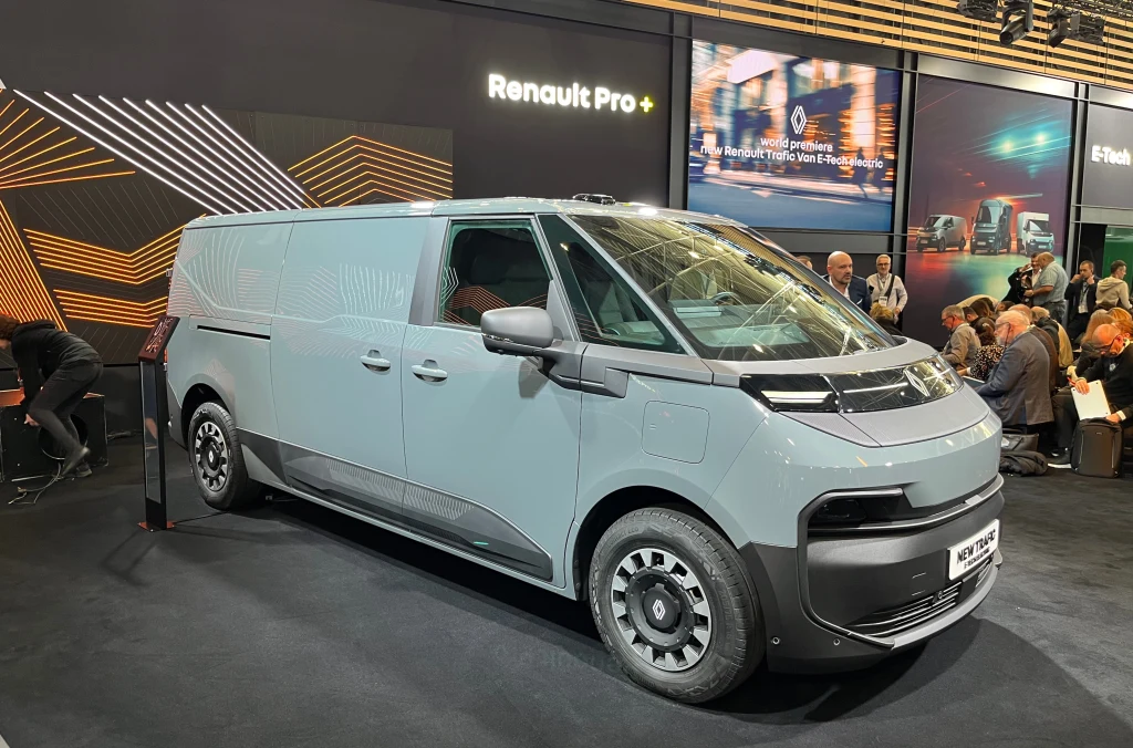 Nowoczesny, szary dostawczy samochód elektryczny Renault stoi na stoisku targowym podczas prezentacji, w otoczeniu ludzi i wyeksponowany pod logotypem Renault Pro+.