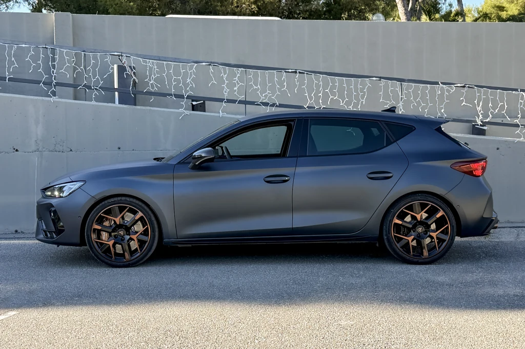 Ciemnoszary hatchback z przyciemnianymi szybami i sportowymi felgami stoi zaparkowany przy betonowej ścianie udekorowanej światełkami.