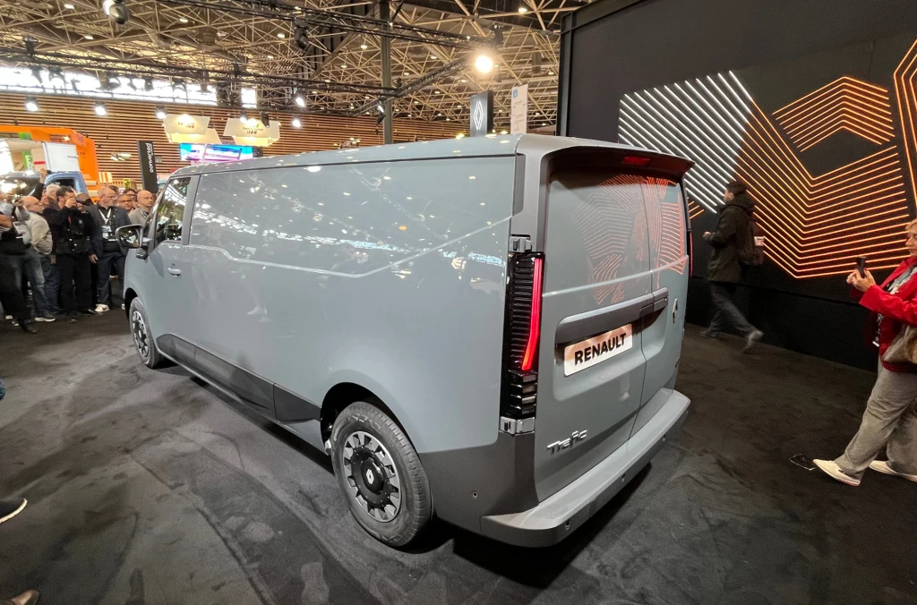 Szary samochód dostawczy marki Renault zaprezentowany w dobrze oświetlonej hali wystawienniczej, otoczony przez odwiedzających i ekspozycję z nowoczesną grafiką na ścianie.