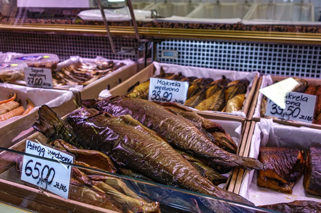 Pstrąg to jedna z najchętniej kupowanych ryb na święta (zdj. ilustracyjne) Witryna chłodnicza z różnymi rodzajami wędzonych ryb, z widocznymi etykietami cenowymi i nazwami gatunków, takimi jak makrela czy pstrąg.