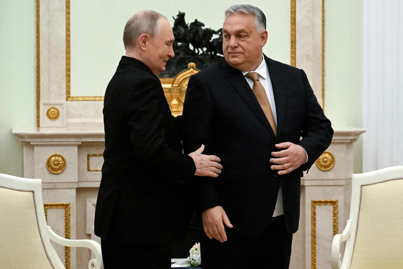 Premier Węgier Viktor Orbán jest promotorem rosyjskich surowców w Europie Środkowo-Wschodniej Dwóch mężczyzn w garniturach stoi naprzeciw siebie w eleganckim, jasnym wnętrzu z ozdobnym kominkiem i rzeźbą w tle. Jeden z nich wykonuje gest zbliżenia się do drugiego, obaj mają poważne wyrazy twarzy.