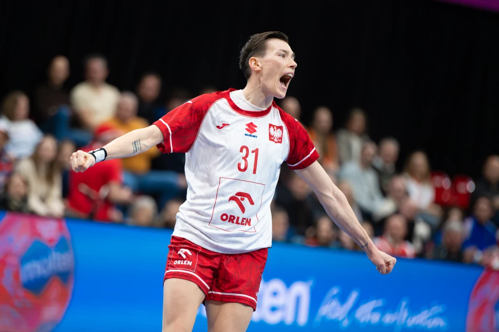 Magda Balsam w meczu z Francją Zawodniczka polskiej reprezentacji piłki ręcznej w trakcie dynamicznej reakcji na boisku, ubrana w czerwono-biały strój z numerem 31 i herbem Polski, w tle widoczna publiczność na trybunach.