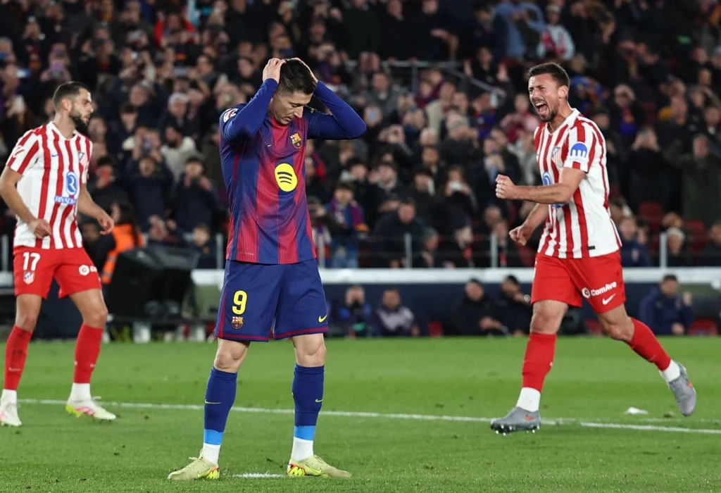 Robert Lewandowski zmarnował rzut karny w starciu z Atletico Madryt Piłkarz Barcelony z numerem 9 w niebiesko-bordowej koszulce trzyma głowę w geście rozczarowania na tle dwóch zawodników Atletico Madryt w biało-czerwonych strojach; w tle widoczna publiczność na trybunach.