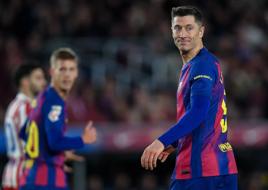Robert Lewandowski, 02.12.2025 r. Piłkarz drużyny FC Barcelona w koszulce w granatowo-bordowych barwach patrzy w stronę aparatu na tle boiska podczas meczu, w tle inni zawodnicy skupieni na grze.