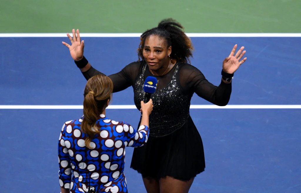 Znana tenisistka na korcie podczas wywiadu po meczu, trzyma ręce uniesione do góry, a dziennikarka w kolorowej sukience z mikrofonem zadaje pytanie.