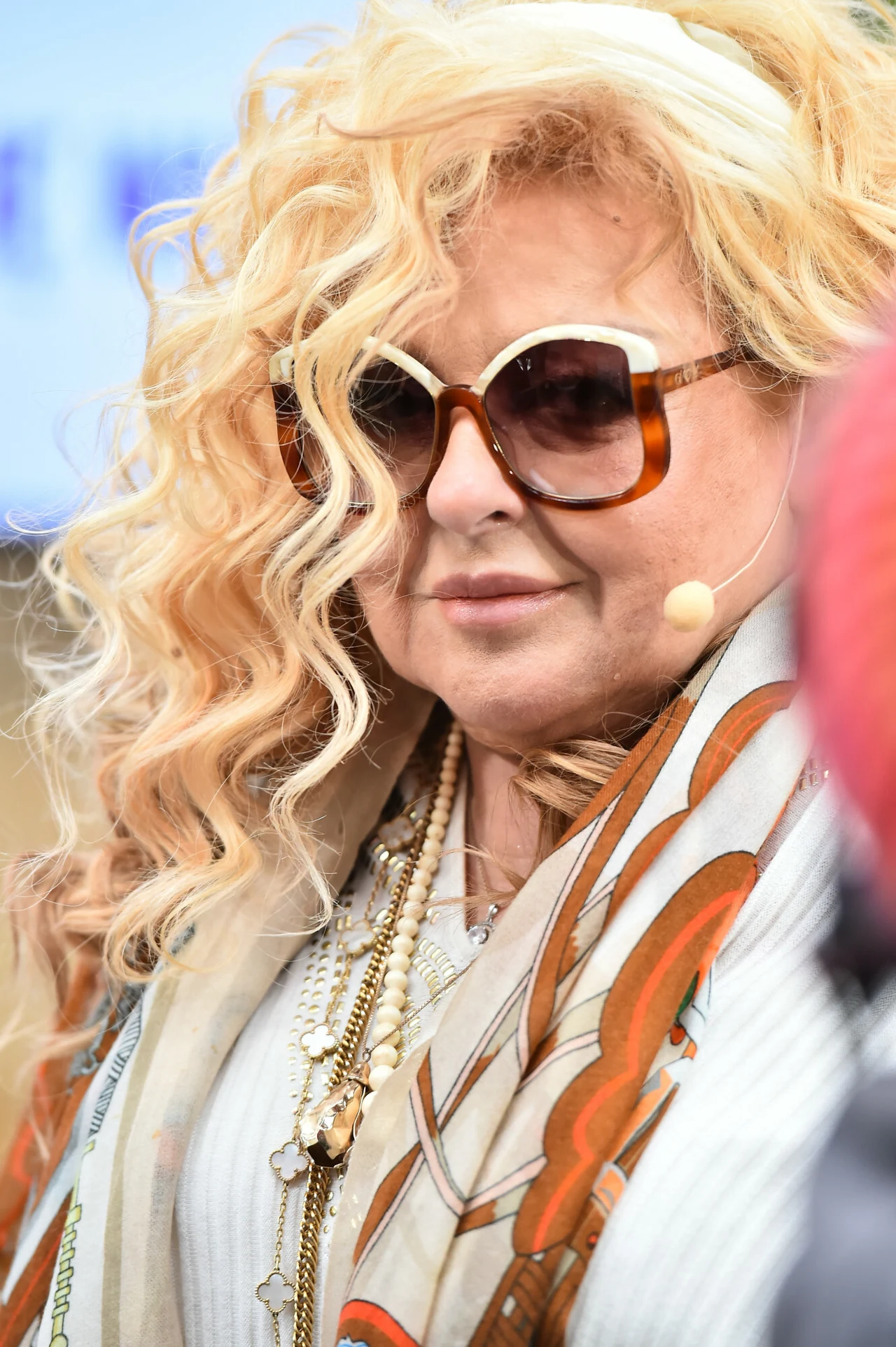 Najbardziej rozpoznawalny dodatek w stylizacjach Magdy Gessler to obfity szal lub chusta Portret kobiety w dużych okularach przeciwsłonecznych, z blond kręconymi włosami, w jasnym szalu z wzorem i licznymi naszyjnikami na szyi. Kobieta ma mikrofon przypięty do twarzy.