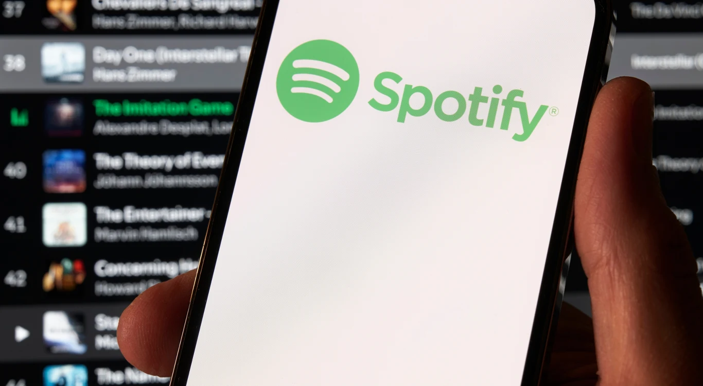 Już niebawem pojawi się kolejna edycja Spotify Wrapped Logo Spotify wyświetlone na ekranie smartfona, w tle niewyraźna lista utworów i artystów na interfejsie aplikacji muzycznej.