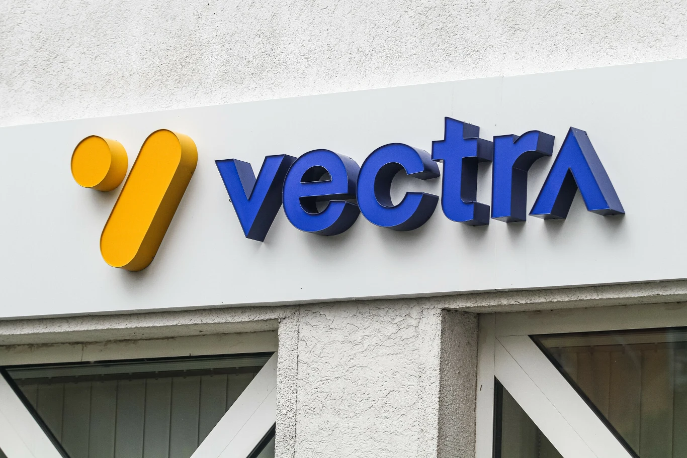 Vectra ukarana przez UOKiK, firma nie zgadza się z decyzją Logo firmy Vectra zamontowane na jasnej elewacji budynku, żółty symbol oraz niebieski napis wokół białego tła, całość nad oknami.