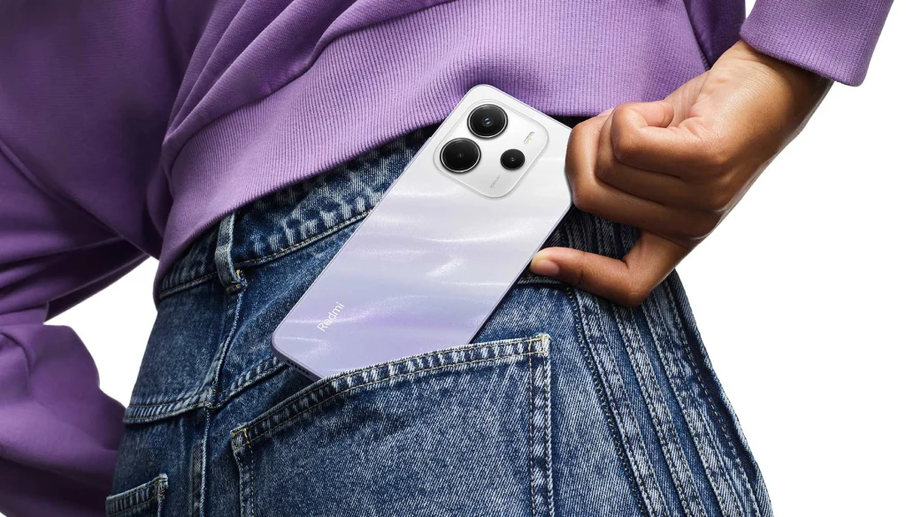 Smartfon z trzema aparatami wkładany do tylnej kieszeni dżinsów przez osobę ubraną w fioletową bluzę.