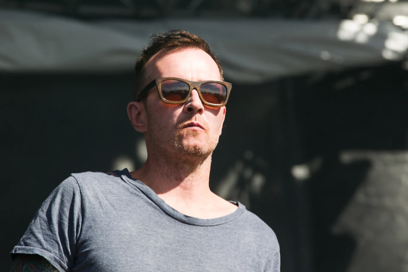 Scott Weiland na pół roku przed śmiercią - 31 maja 2015 r., Napa w Kalifornii Mężczyzna w ciemnych okularach przeciwsłonecznych, ubrany w szarą koszulkę, stoi na tle rozmytego, ciemnego tła, w jasnym świetle dziennym. Wyraz jego twarzy jest poważny, a włosy zaczesane do góry.