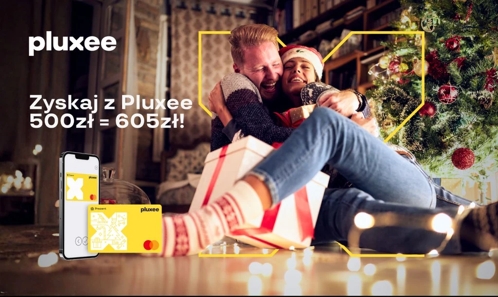 Para w ciepłej, domowej atmosferze obejmuje się przy choince, w otoczeniu świątecznych dekoracji, prezentów oraz wyświetlonych kart i telefonu z aplikacją pluxee.