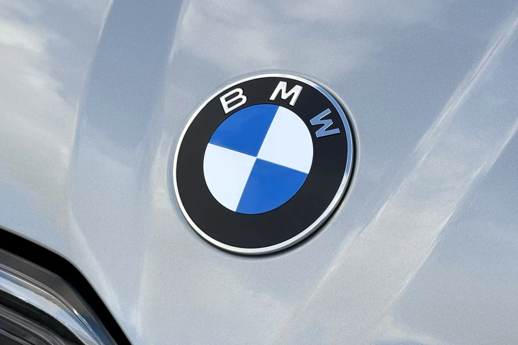 Ceny nowego BMW iX3 zaczynają się od 310 tys. zł. Obecnie auto dostępne jest w jednym wariancie napędowym. W przyszłości pojawią się kolejne wersje, w tym podstawowa. Logo marki BMW na srebrnym tle maski samochodu, charakterystyczne kolory niebiesko-biało-czarne na okrągłej emblematce.