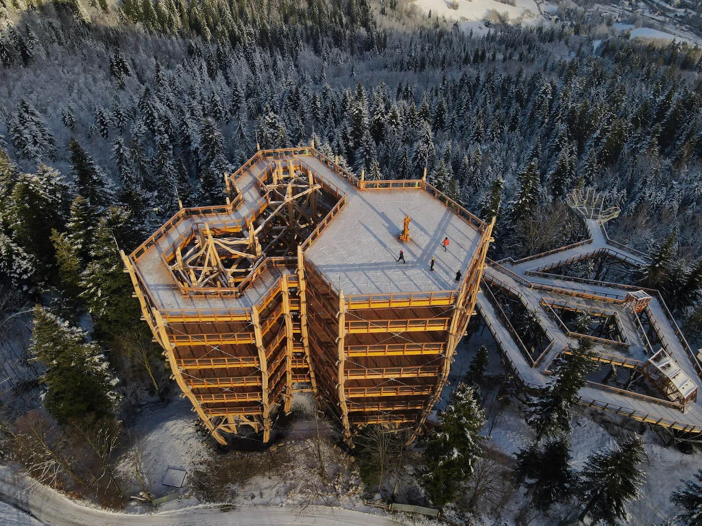 Nowa wieża widokowa w Wiśle została udostępniona mieszkańcom i turystom / fot. wiezawidokowa.pl Nowoczesna, wielopoziomowa wieża widokowa z drewna w otoczeniu zaśnieżonego lasu, z wyraźnie widoczną konstrukcją i platformami spacerowymi oraz zimowym krajobrazem rozciągającym się wokół.