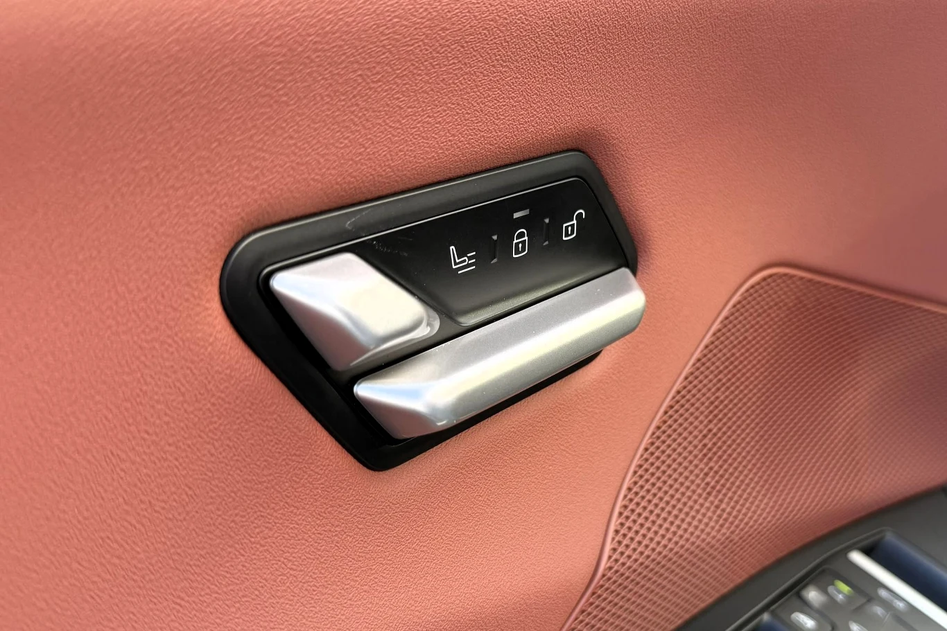 Panel sterowania fotelem samochodowym na tle różowej tapicerki drzwi, z widocznymi przyciskami do ustawiania pozycji siedzenia i regulacji blokady.