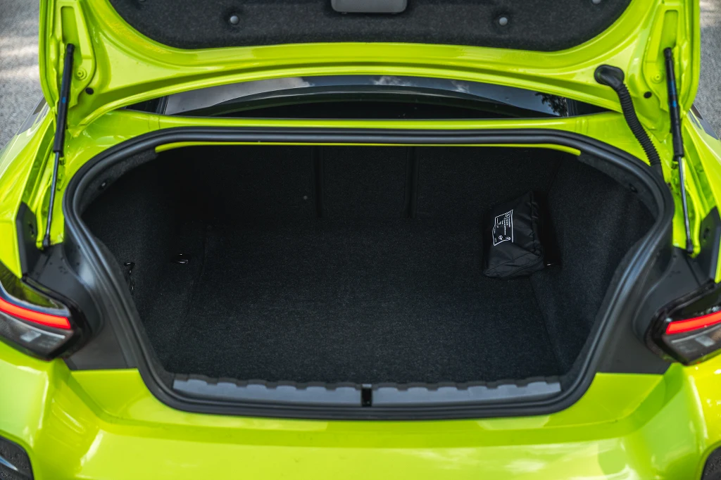 Otwarty bagażnik jasnozielonego samochodu osobowego, wnętrze bagażnika jest puste z wyjątkiem niewielkiej czarnej torby po prawej stronie.