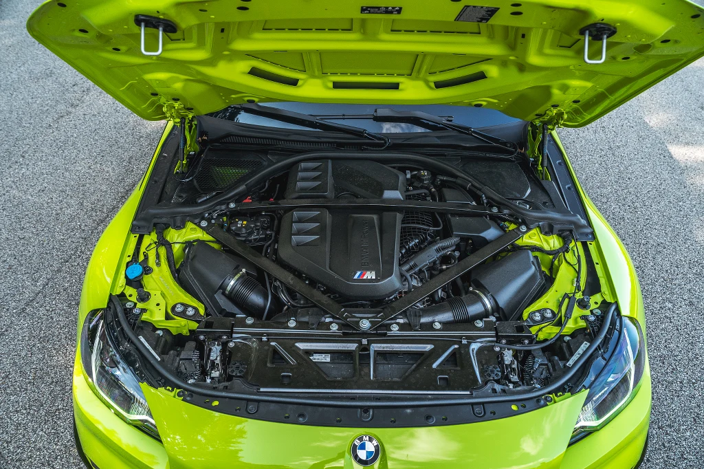 Silnik sportowego samochodu marki BMW z podniesioną maską, widoczna konstrukcja komory silnika oraz elementy mechaniczne auta w jaskrawym, żółto-zielonym kolorze nadwozia.