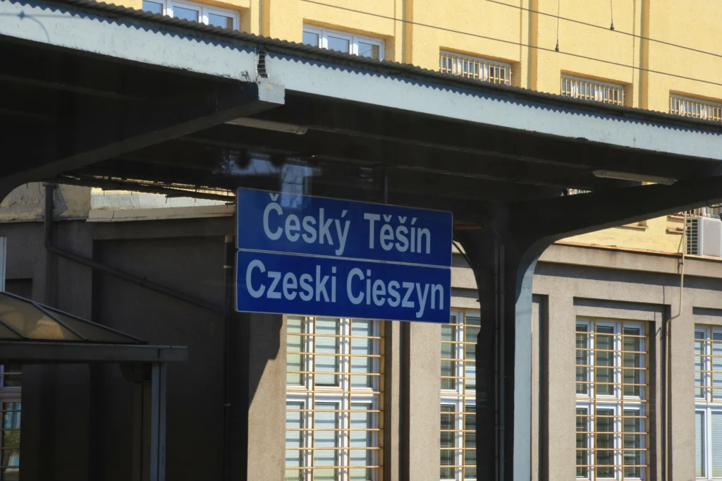 Mieszkaniec Czeskiego Cieszyna chwalił Polskę za to, jak się rozwinęła Dwujęzyczna tablica informacyjna z napisem České Těšín oraz Czeski Cieszyn zamontowana na peronie kolejowym, w tle elewacja budynku z licznymi oknami i klimatyzatorem.