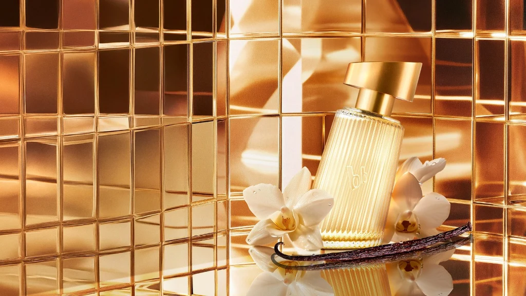 Flakon perfum w złotej oprawie, otoczony białymi kwiatami orchidei oraz laską wanilii, odbijający światło i złote refleksy w tle.