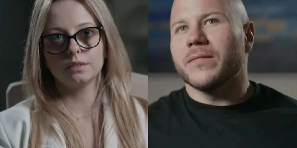 Dwie osoby w średnim planie siedzą naprzeciwko siebie, kobieta z długimi blond włosami i okularami oraz mężczyzna o krótkich włosach i brodzie, oboje patrzą poważnie w stronę aparatu.