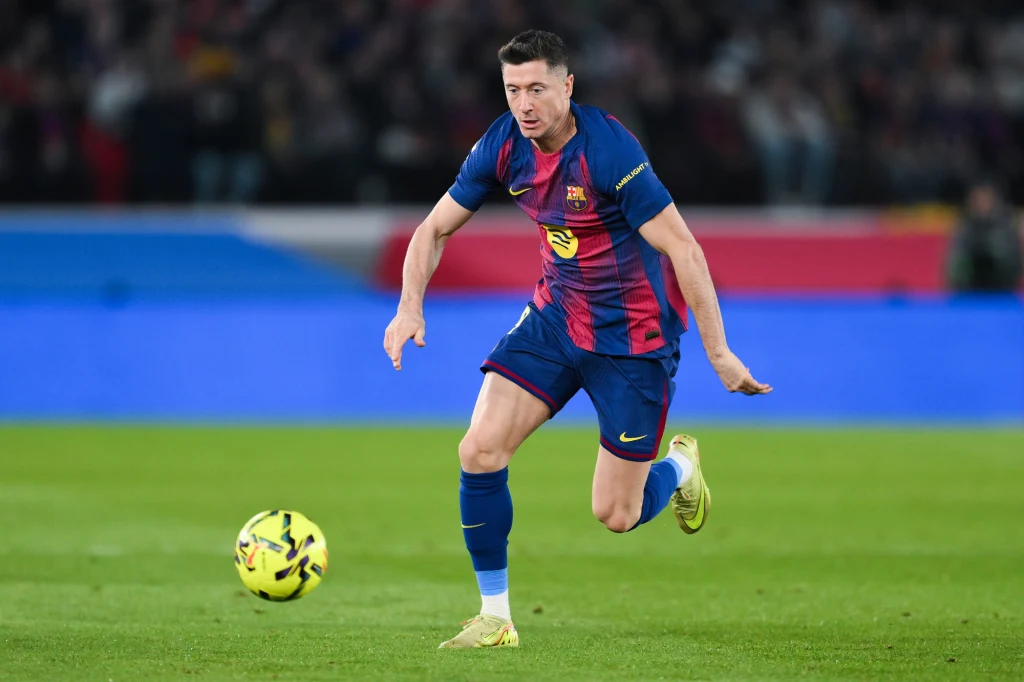 Robert Lewandowski w barwach FC Barcelona podczas meczu La Liga 2025/2026 Piłkarz w stroju FC Barcelony biegnie po boisku z piłką przy nodze, skupiony na akcji meczowej, w tle widoczni kibice oraz fragmenty stadionu.