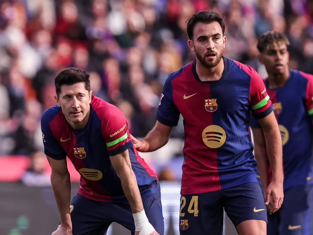 Piłkarze FC Barcelony w granatowo-bordowych strojach zespołu podczas meczu na stadionie, skupieni na boiskowych wydarzeniach, w tle rozmyta publiczność.