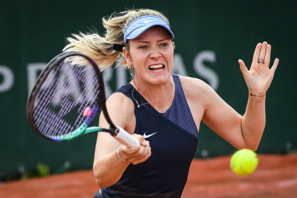 Katharina Hobgarski Tenisistka w niebieskiej sportowej koszulce i daszku wykonuje dynamiczne uderzenie forehandem na ziemnym korcie, skupiając się na żółtej piłce tenisowej.