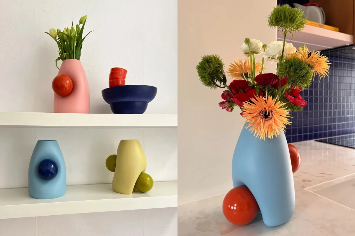 Kolorowe, geometryczne wazony o organicznych kształtach ustawione na półce i na blacie, ozdobione elementami w kontrastowych kolorach. W jednym z wazonów znajduje się kompozycja świeżych kwiatów w różnych barwach.