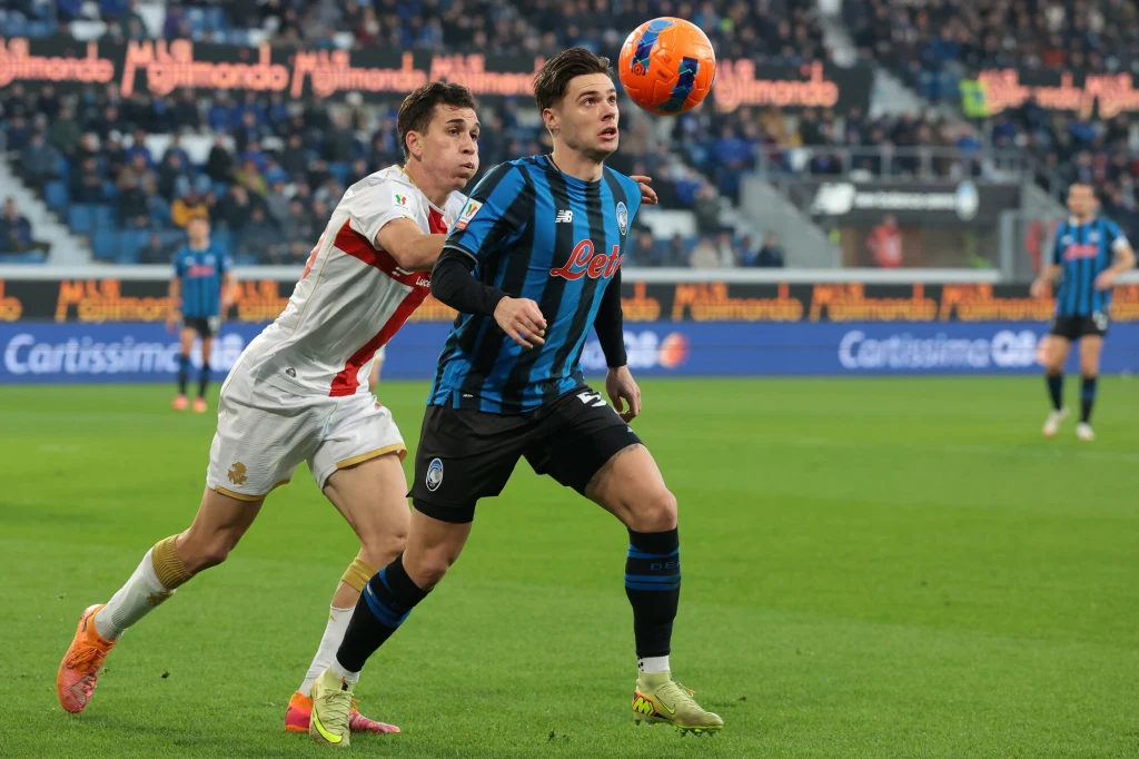 Nicola Zalewski podczas meczu Atalanta - Genoa Dwóch piłkarzy rywalizuje o piłkę na murawie, zawodnik w biało-czerwonym stroju próbuje przejąć piłkę od gracza w niebiesko-czarnej koszulce. W tle rozmyta publiczność na trybunach stadionu.